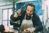 Trabajador metalúrgico masculino martillando metal en taller de forja - foto de stock