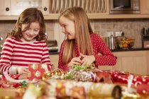 Zwei Mädchen wickeln Weihnachtsgeschenke am Tisch ein — Stockfoto