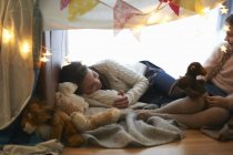 Two sisters in bedroom den lying down with soft toys — Stock Photo