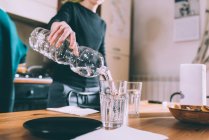 Schnappschuss von junger Frau, die Wasser auf Küchentisch gießt — Stockfoto