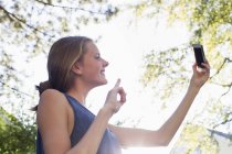 Teenage girl posing for smartphone selfie in park — Stock Photo
