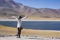 Back view of tourist woman with hands up at lake in San Pedro de Atacama, Chile — Stock Photo