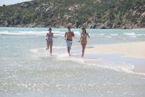 Amigos corriendo en olas en la playa - foto de stock