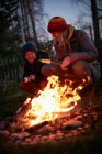 Mature woman and son toasting marshmallows on garden campfire at dusk — Stock Photo
