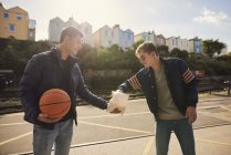 Joven compartiendo bolsa de papas fritas con un amigo, joven sosteniendo baloncesto, Bristol, Reino Unido - foto de stock