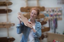 Frau arbeitet in Skateboardladen und inspiziert Holzbrett — Stockfoto