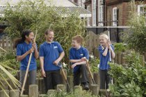 Group of four school children with gardening tools — Stock Photo