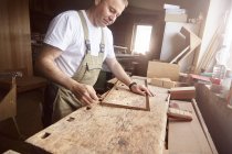 Боковой вид человека плотника в фартуке, работающего с деревянными досками — стоковое фото