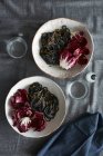Top view of squid ink spaghetti dish and radicchio lettuce salad — Stock Photo