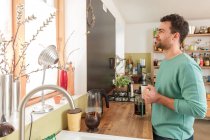 Mann in Küche hält Kaffeetasse und schaut aus Fenster — Stockfoto