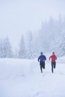 Happy sportive man and woman jogging in snow covered forest, Gstaad, Switzerland — Stock Photo