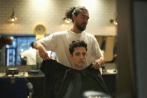 Barbiere mettere abito su cliente maschile in negozio di barbiere — Foto stock