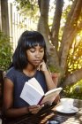 Junge Frau sitzt draußen, liest Buch, Kaffee vor sich — Stockfoto