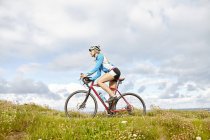 Cyclist riding past meadow on sunny day — Stock Photo