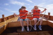 Двоє дітей сидять у човні в рятувальних жилетах і тримають мотузку — стокове фото