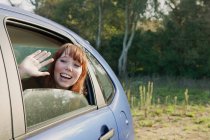 Adolescente chica saludando desde el asiento trasero del coche - foto de stock