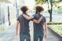 Вид сзади на идентичных взрослых близнецов мужского пола, прогуливающихся по тротуару — стоковое фото