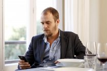 Mann sitzt am Esstisch und benutzt Smartphone — Stockfoto