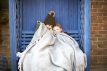 Frères et sœurs enveloppés dans une couverture reposant sur un banc de tonnelle — Photo de stock