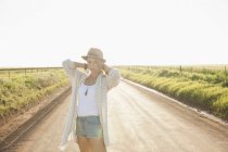 Mid adult woman on country road, arms behind neck, looking at camera — Stock Photo