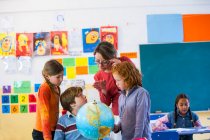 Professeur d'école primaire et écoliers regardant le globe en classe — Photo de stock