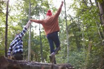 Casal na floresta segurando as mãos equilibrando na árvore caída — Fotografia de Stock