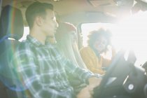 Tres amigos adultos jóvenes conduciendo en coche iluminado por el sol - foto de stock