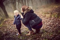 Femme adulte moyenne accroupie avec tout-petit fils dans la forêt d'automne — Photo de stock