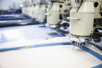 Rows of programmed embroidery machines speed stitching white cloth in clothing factory — Stock Photo