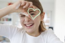 Girl looking through heart shaped cookie cutter smiling — Stock Photo