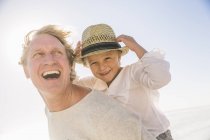 Padre dando hijo a cuestas sonriendo, usando sombrero de sol de paja - foto de stock