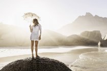 Woman standing on rock with parasol on sunlit beach, Cape Town, South Africa — Stock Photo