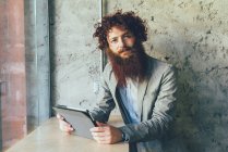 Portrait of young male hipster with curly red hair and beard in office — Stock Photo