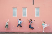 Friends jumping against pink wall background — Stock Photo