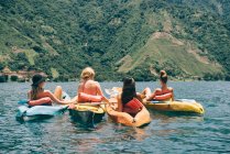 Vista trasera de cuatro amigas jóvenes haciendo kayak en el lago Atitlán, Guatemala - foto de stock