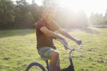 Portrait of young man on bicycle in sunlit park — Stock Photo