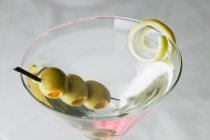 Martini drink with olives and lemon peel in glass — Stock Photo