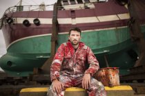 Retrato do pintor masculino sentado em frente ao barco de pesca na doca seca — Fotografia de Stock