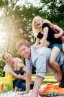 Father giving daughters piggyback at family picnic in park — Stock Photo
