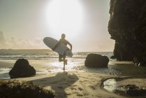 Homme mûr courant vers la mer, tenant planche de surf — Photo de stock