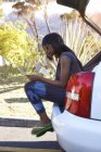 Молодая женщина, сидящая в багажнике открытой машины, глядя на цифровой планшет — стоковое фото