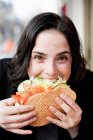 Жінка гризе сендвіч і дивиться на камеру — стокове фото