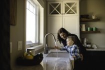 Mãe ajudando filho criança lavar as mãos na pia da cozinha — Fotografia de Stock