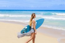 Mujer joven paseando en la playa llevando tabla de surf, República Dominicana, El Caribe - foto de stock