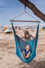 Дівчина штовхає брата в гамак на пляжі — стокове фото