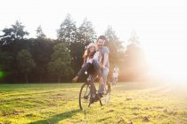 Young woman on handlebars of boyfriends bicycle at party in park — Stock Photo