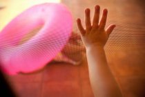 Дитяча рука торкається сітки екрану, рожеве надувне кільце на фоні — стокове фото