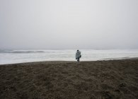 Young woman wrapped in blanket walking on misty beach — Stock Photo