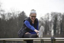 Frau mit erhobenem Bein auf Geländer beugt sich nach vorne — Stockfoto