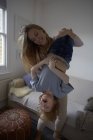 Середня доросла жінка тримає сина догори ногами у вітальні — стокове фото